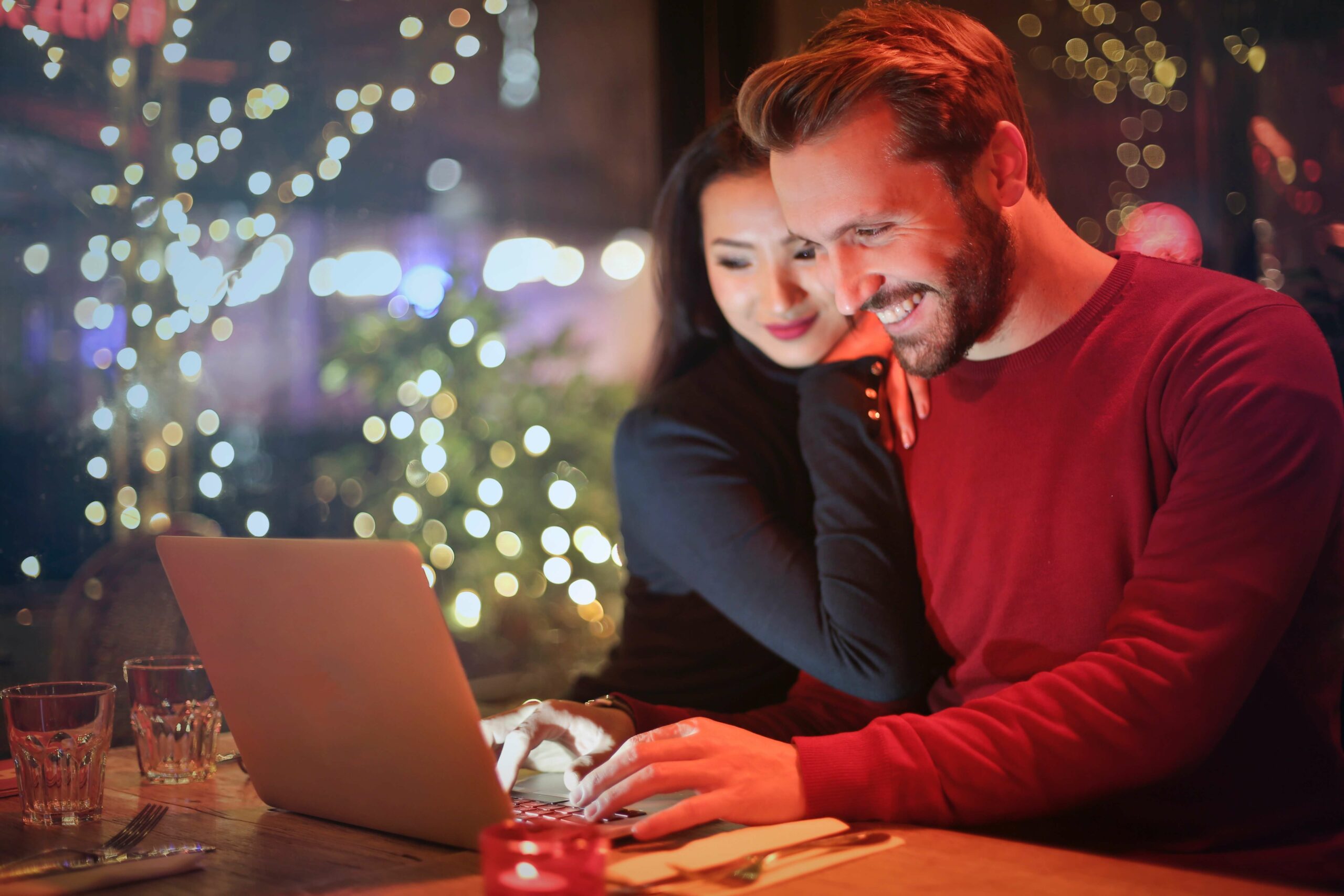 man and woman smiling at a computer in front of a Christmas tree