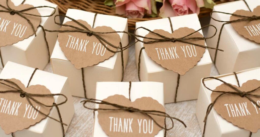 A table display of small, boxed bridal shower favors wrapped with brown string and heart-shaped "thank you" cards.