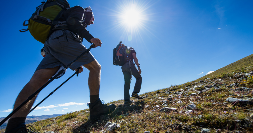 Two hikers make their way up a grassy and stony incline together.